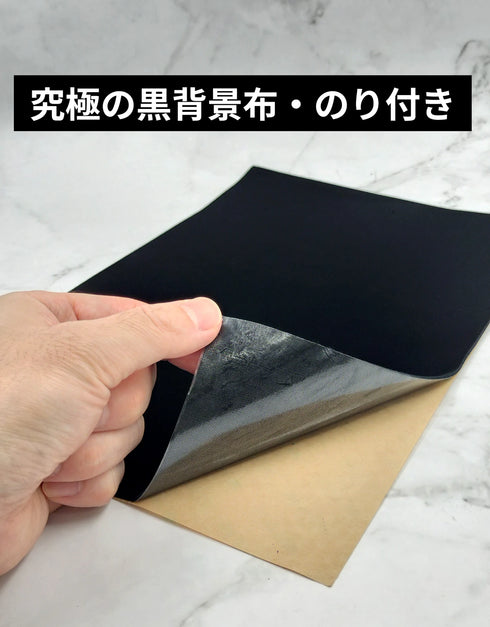 特級暗黒布 太黒門(糊付き)の裏面にある粘着シールの剥離紙をめくっている様子。強力な粘着面により、壁面などへ直接貼り付けて施工できることを示す商品写真
